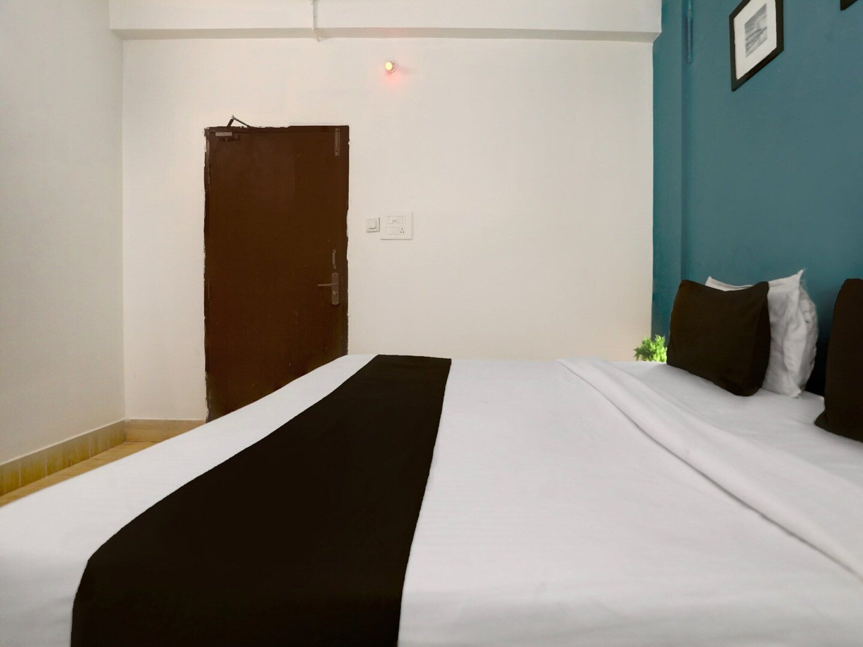 A hotel room with a bed, a door, and a wall-mounted light fixture.