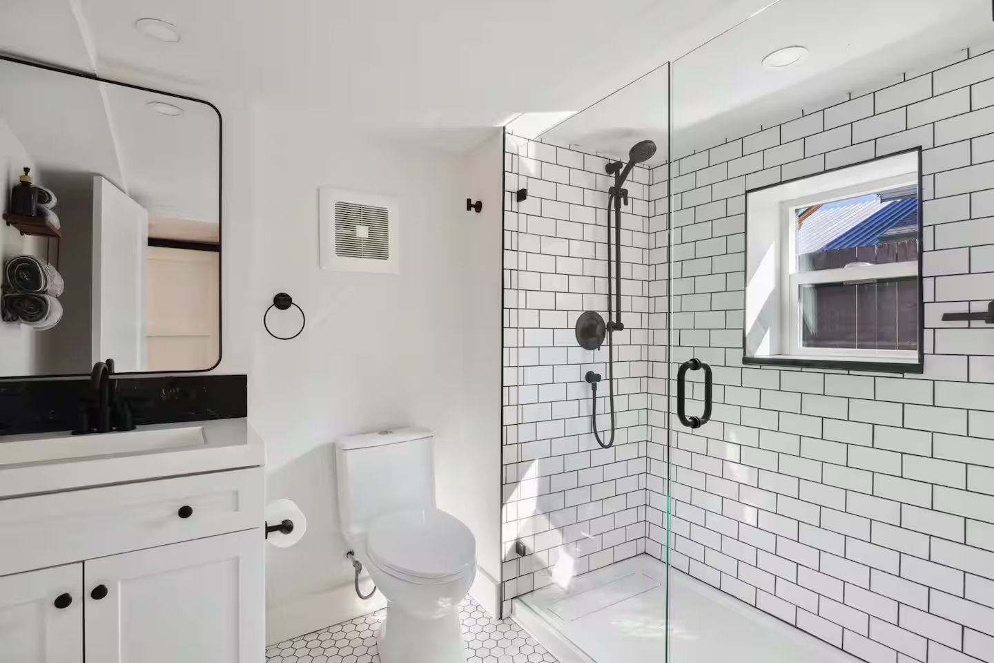 A modern bathroom with a white toilet, a glass-enclosed shower, and a large mirror.