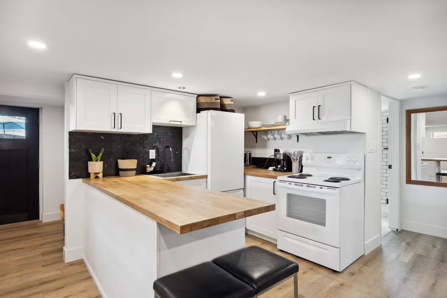 A modern kitchen with white cabinetry, a wooden countertop, and a black backsplash.