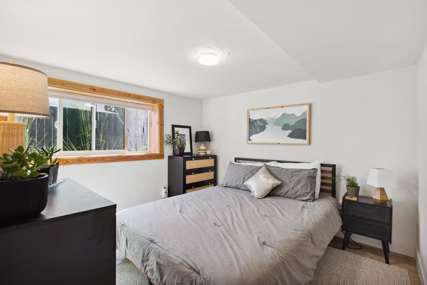 Une chambre à coucher comprenant un lit, des tables de chevet, une commode, une fenêtre avec vue et un luminaire au plafond.