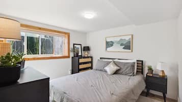 Une chambre à coucher comprenant un lit, des tables de chevet, une commode, une fenêtre avec vue et un luminaire au plafond.