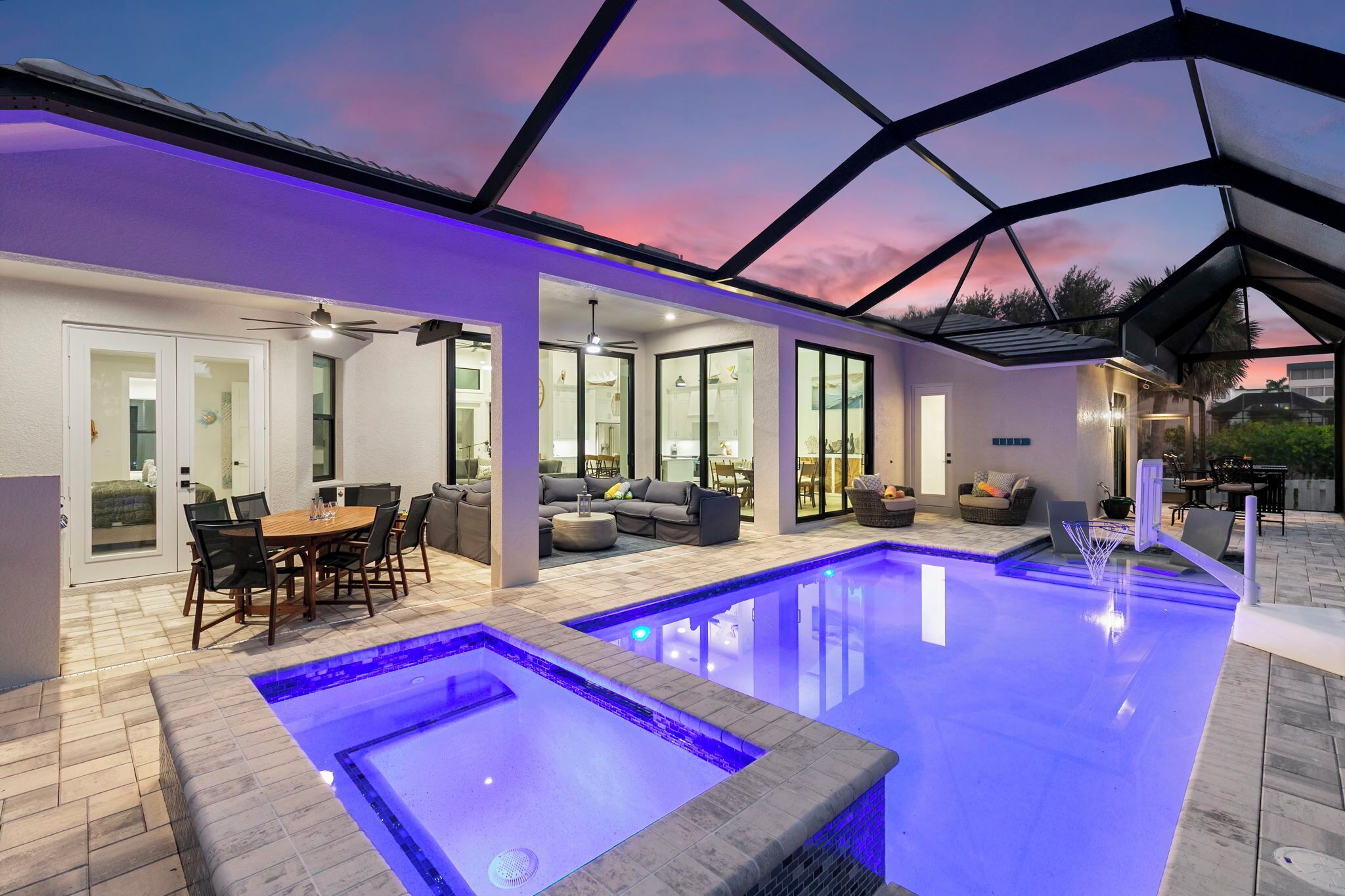 A modern indoor pool area with a glass-enclosed patio, a dining area, and a seating arrangement.