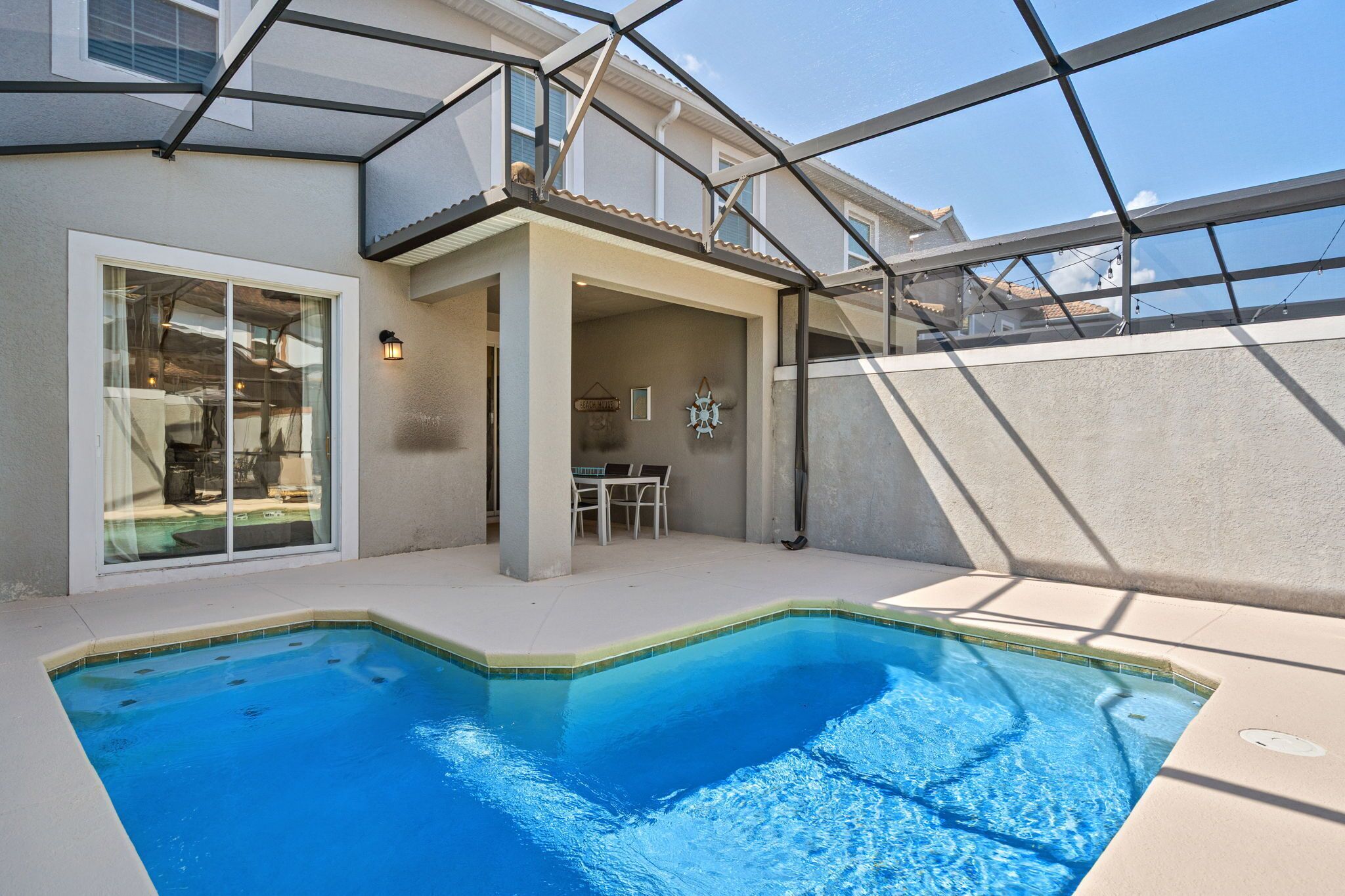 Una piscina con cerramiento de vidrio, un comedor con sillas y un aplique de pared.