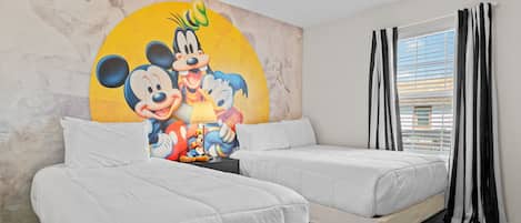 A hotel room with two beds, a Mickey Mouse mural on the wall, and a window with curtains.