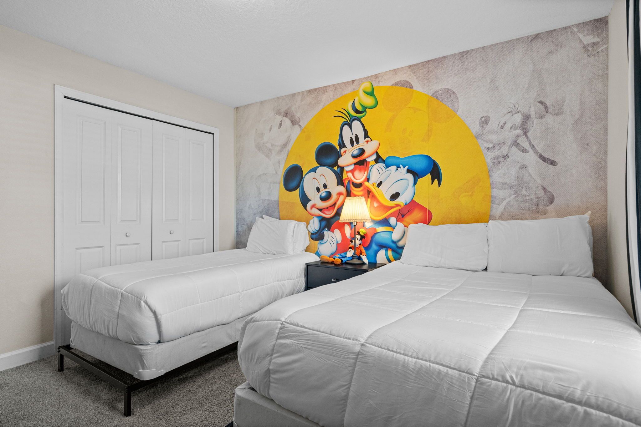 Une chambre d’hôtel avec deux lits simples, une grande fresque représentant Mickey et Minnie, et une porte blanche.