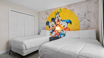 Une chambre d’hôtel avec deux lits simples, une grande fresque représentant Mickey et Minnie, et une porte blanche.