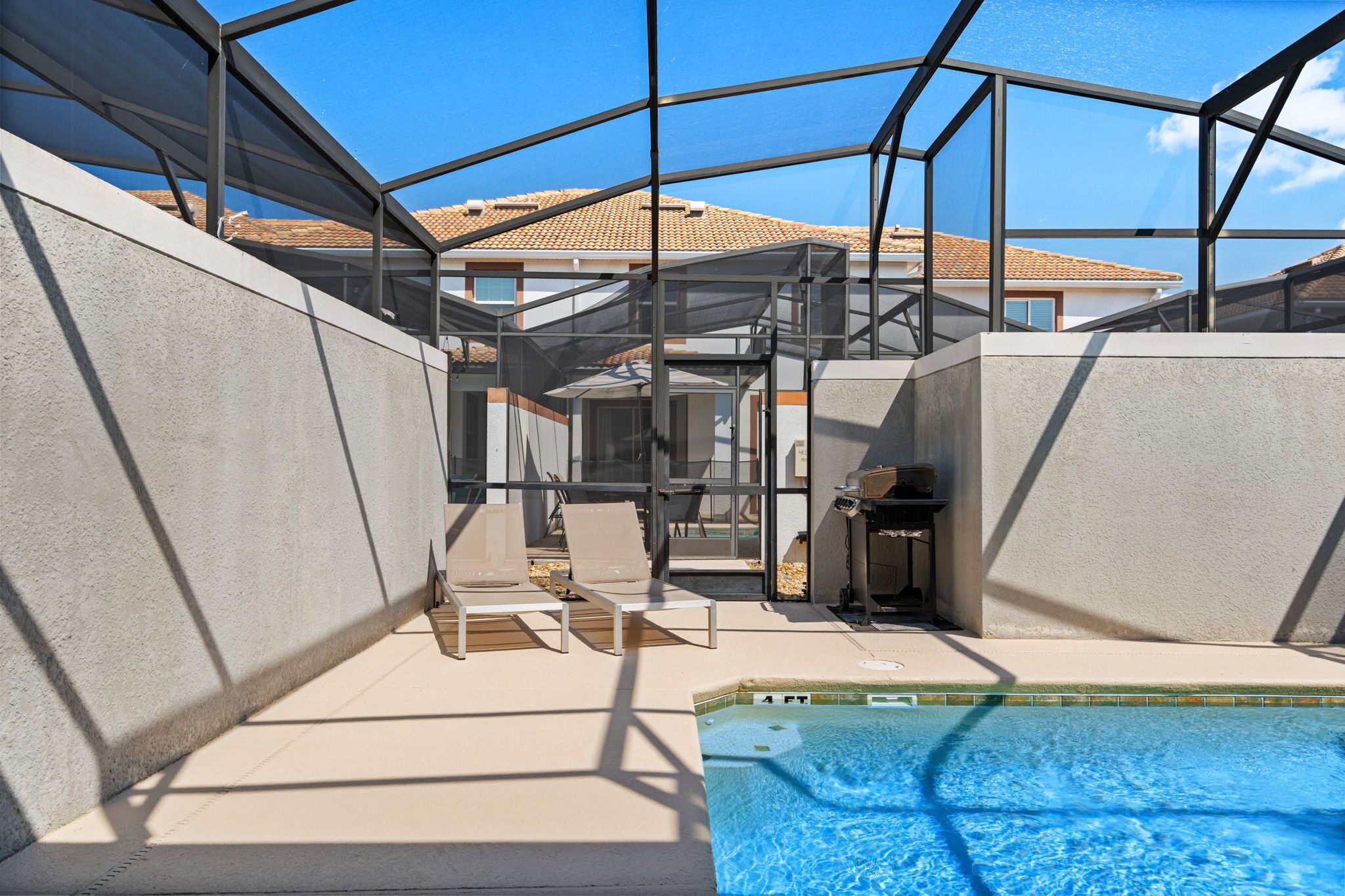 A pool area with a glass enclosure, lounge chairs, and a barbecue grill.