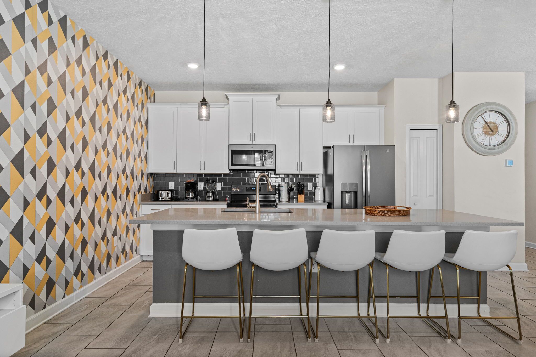 Une cuisine moderne dotée d’un îlot central, de tabourets de bar, d’appareils électroménagers en acier inoxydable et d’un revêtement mural à motifs géométriques.