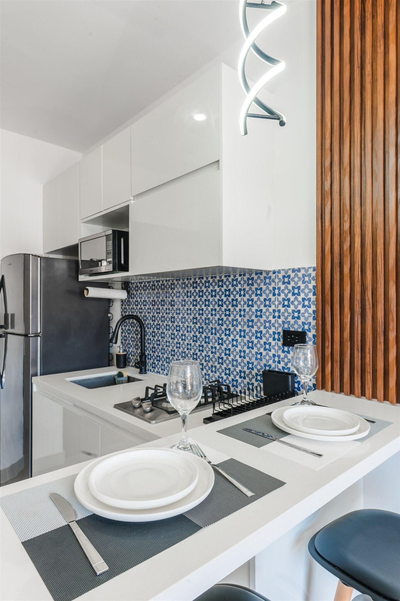Una cocina moderna con gabinetes blancos, un refrigerador de acero inoxidable, un microondas y un salpicadero con diseño azul.
