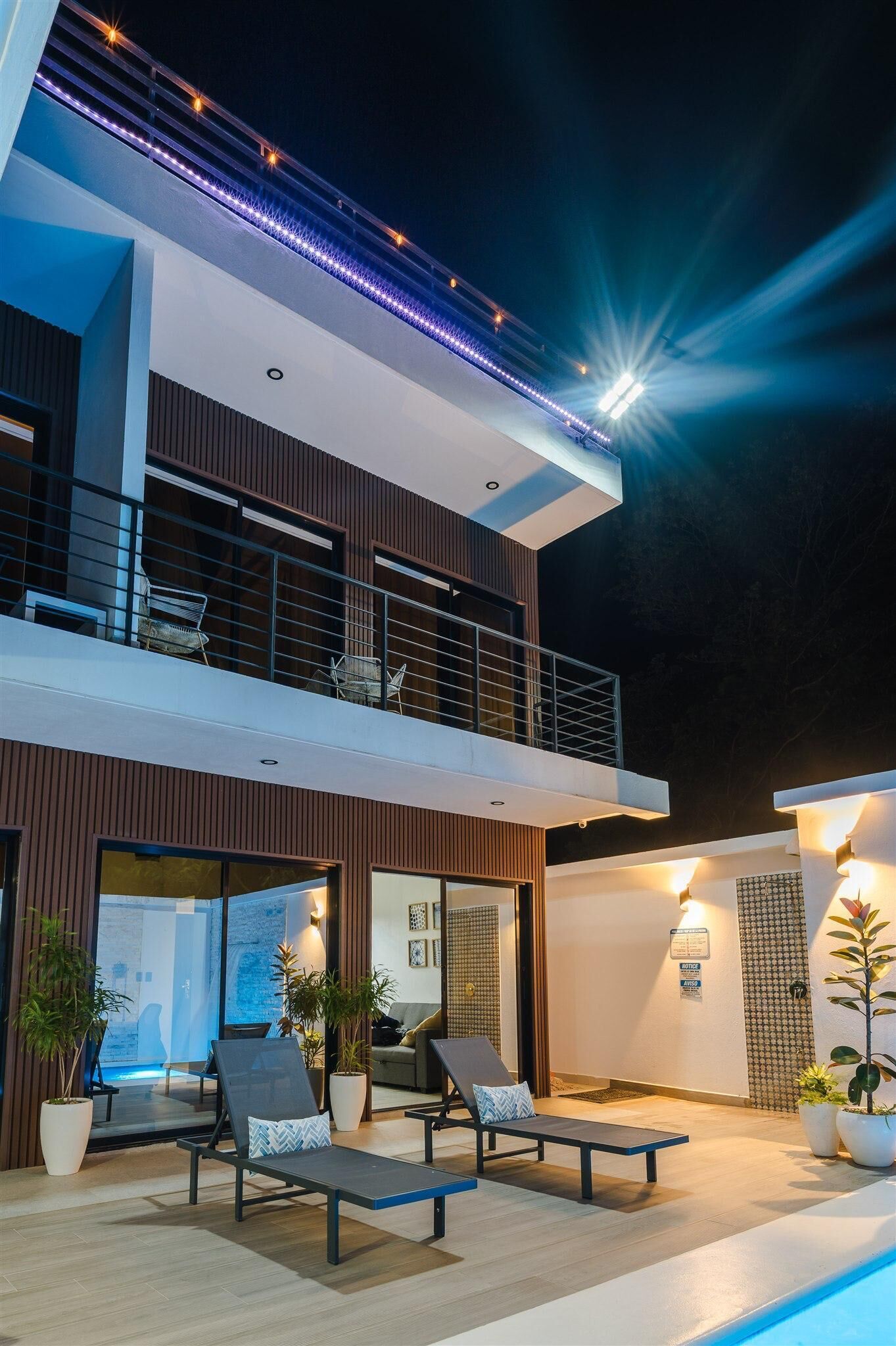 Een modern huis met twee verdiepingen, een balkon, zitplaatsen buiten en een zwembad.