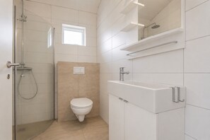 A modern bathroom with a glass shower enclosure, a toilet, and a sink with a mirror above.