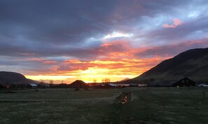 A rural landscape with a sunset, open fields, and distant houses.