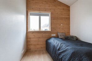 A bedroom with a wooden slatted wall, a bed with a quilted cover, a window, and a small bedside table.
