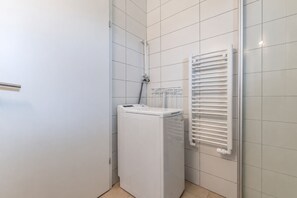 A bathroom with a white tiled wall, a white radiator, and a white washing machine. - Cozy modern cottage w/Hot Tub & Sauna Mountain view (Kjósarhreppur)