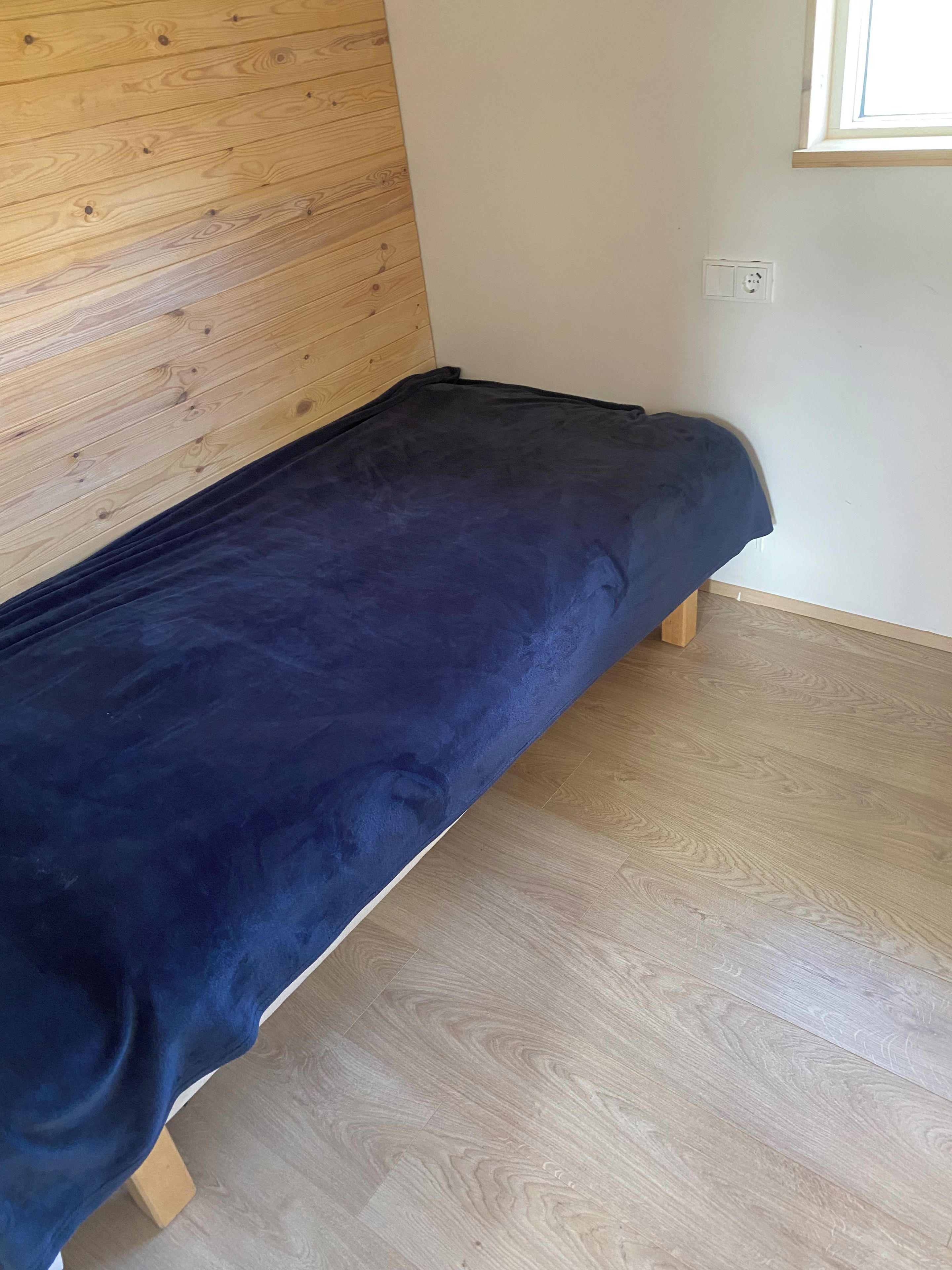 A single bed with a dark cover in a room with wooden flooring and a wooden headboard.