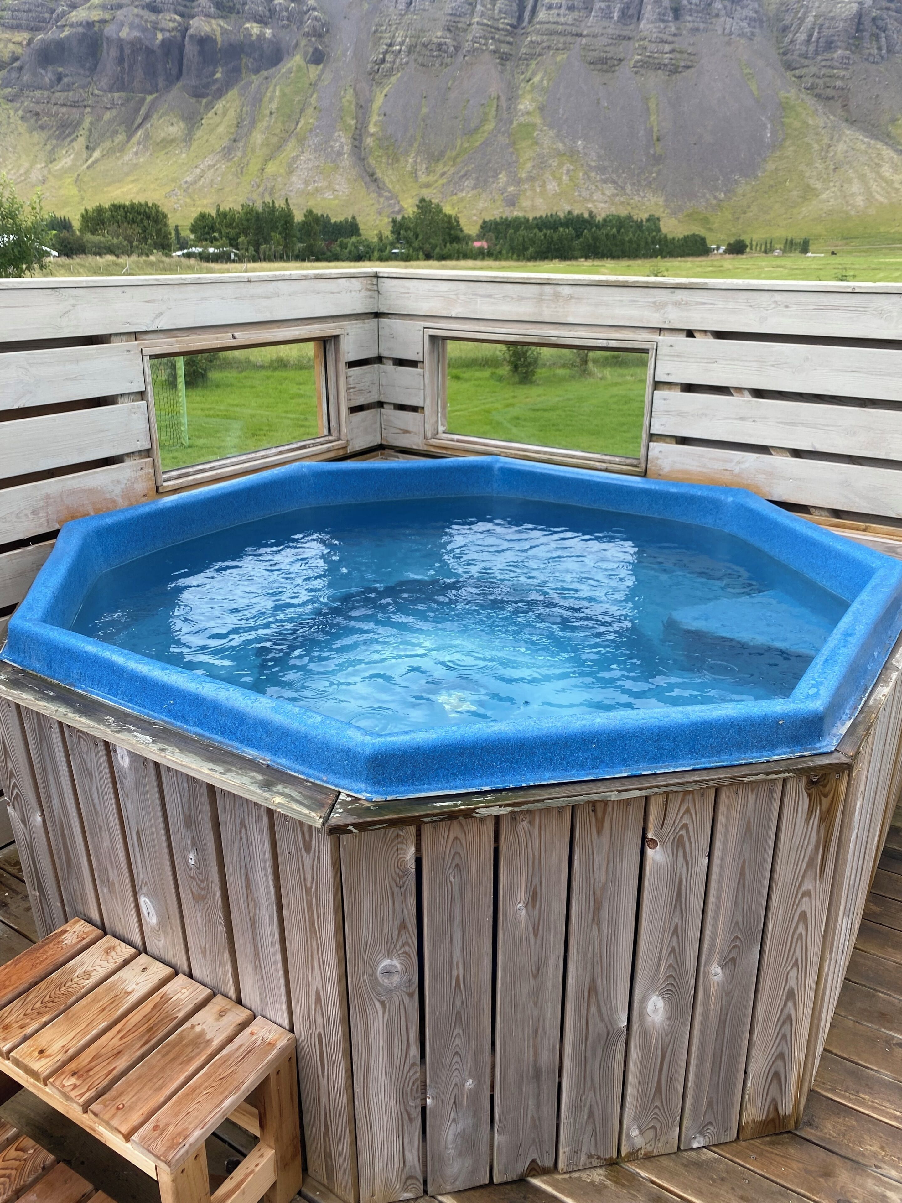 A wooden hot tub on a deck with a view of a mountainous landscape.