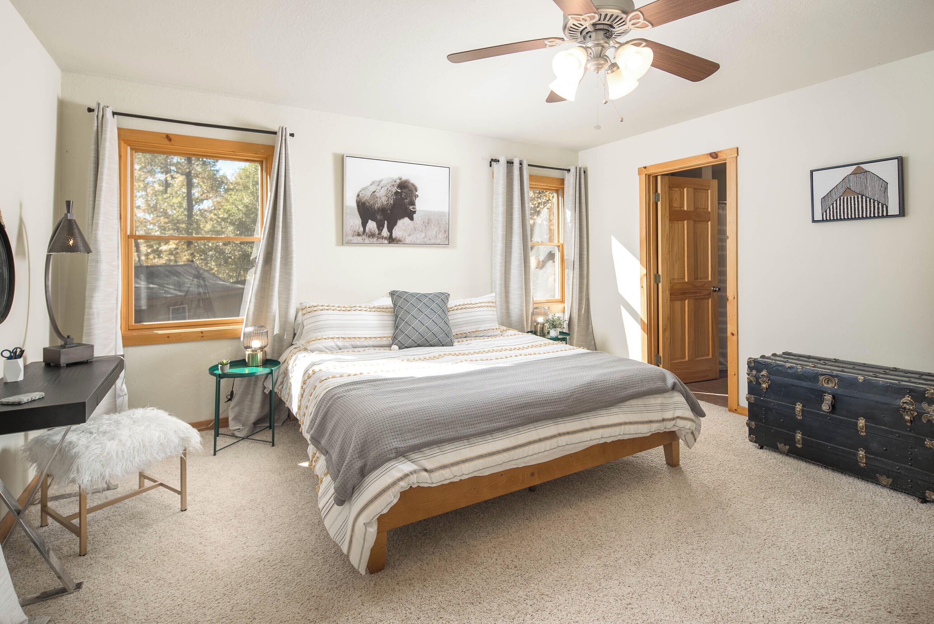 A bedroom with a bed, a desk, a chair, a ceiling fan, and a door.