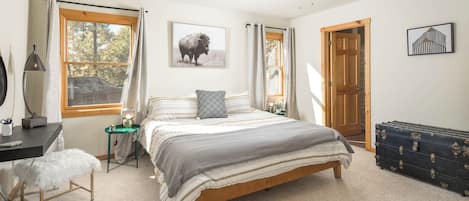 A bedroom with a bed, a desk, a chair, a ceiling fan, and a door.