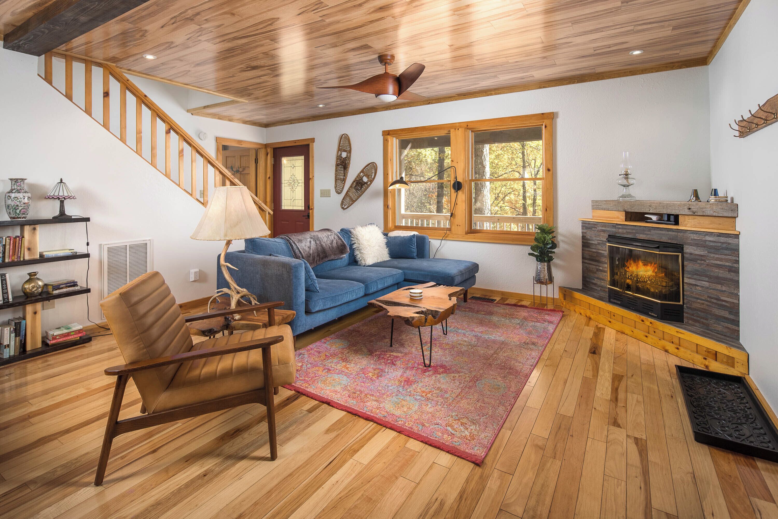 A cozy living room with a wooden staircase, a blue sofa, a fireplace, and a bookshelf.