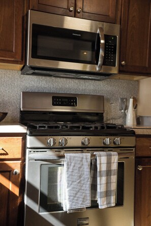 A kitchen with a stainless steel microwave and oven, wooden cabinets, and a tiled backsplash. - Whisper Ridge 3BR Deep Gap Cabin · Mountain Views · Fire Pit · Sleeps 9 (Watauga County)