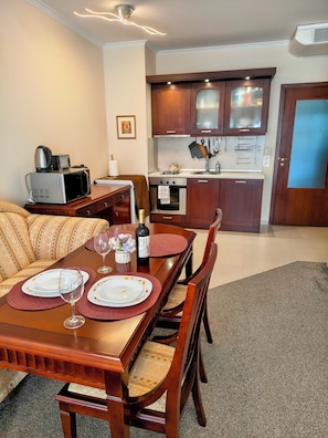 A dining area with a wooden table set for two, a sofa, and a kitchenette in the background. - Delightful 2-bedroom apartment with AC in charming Bansko (Bansko)