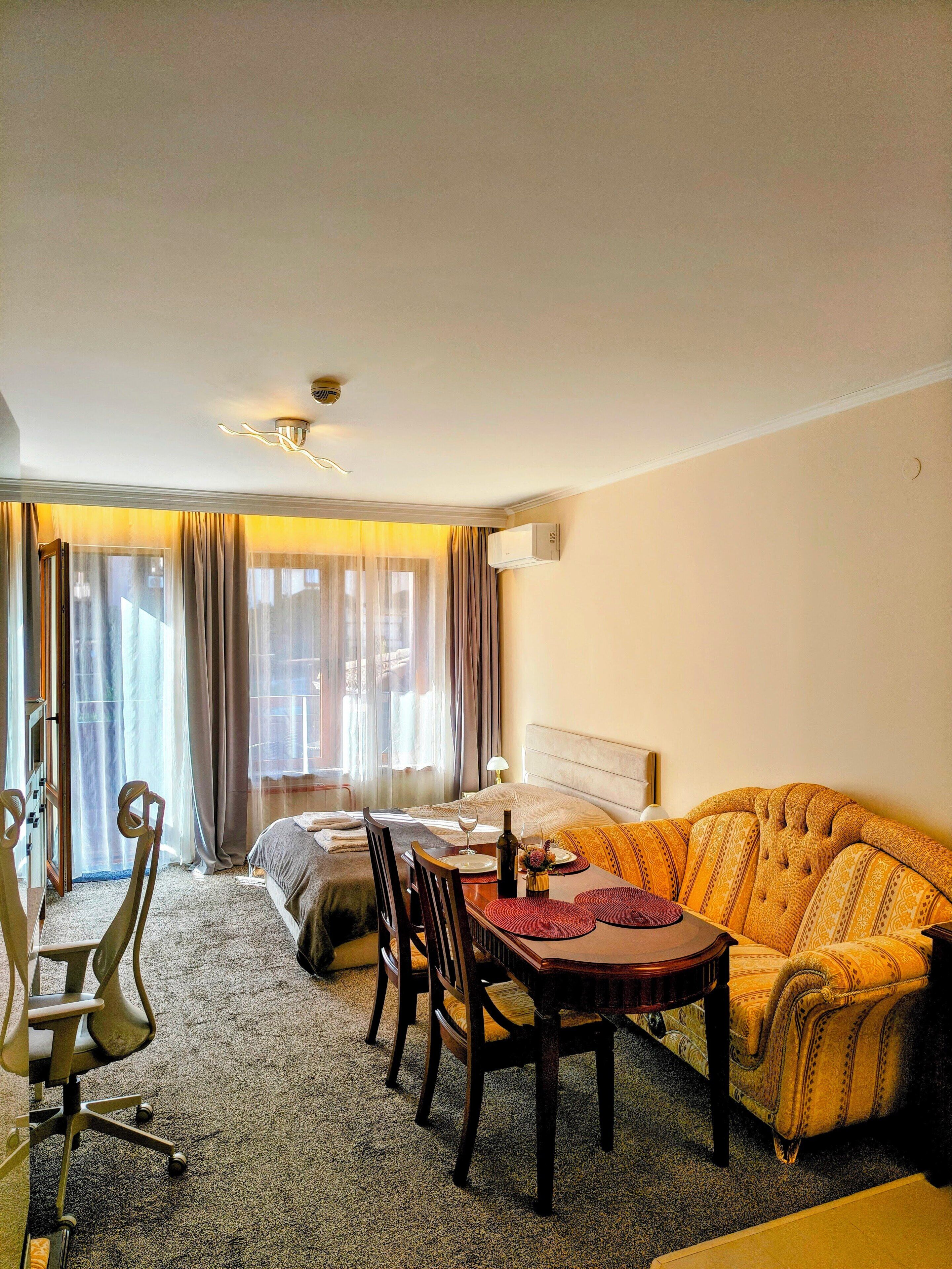 A hotel room with a bed, a sofa, a dining table with chairs, and a window with curtains.