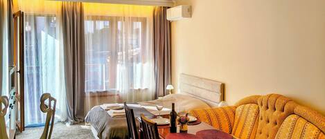 Una habitación de hotel con cama, sofá, mesa de comedor con sillas y una ventana con cortinas.