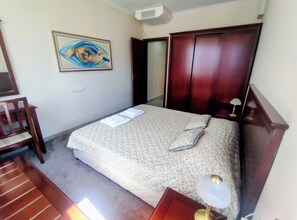 A hotel room with a bed, a chair, a desk, a desk lamp, a painting, and a wardrobe. - Delightful 2-bedroom apartment with AC in charming Bansko (Bansko)