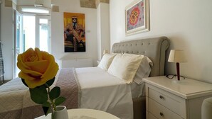 Een slaapkamer met een bed, nachtkastje, lamp en een vaas met een enkele bloem.