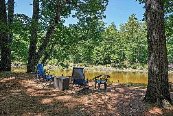 A campsite with two chairs and a table, surrounded by trees and a calm lake.