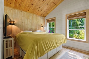 Quarto com cama, luminárias de cabeceira, espelho e janela com vista para vegetação.