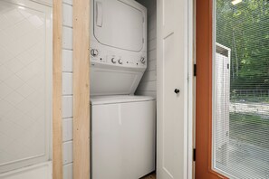 A laundry room with a white washing machine and dryer, a wooden door frame, and a door with a window.
