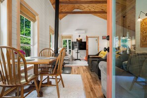A dining area with wooden chairs and a table, a kitchen with a stove and cabinets, and a living area with a couch and a TV.