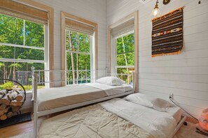 A room with a bunk bed, large windows, a wooden log display, and a wall-mounted light fixture.