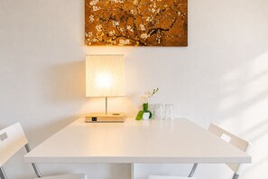 A white dining table with a lamp, a vase with flowers, and two glasses.