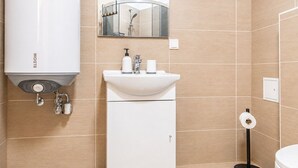 A bathroom with a white sink, a mirror above it, a toilet, and a wall-mounted heater.