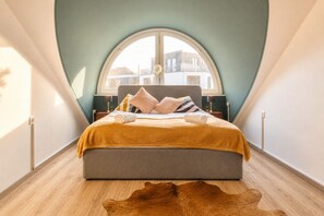 A bedroom with a large bed, a window, and a wooden floor.