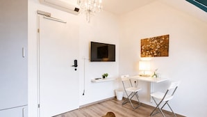 A modern room with a flat-screen TV, a desk with two chairs, a chandelier, and a mounted artwork.