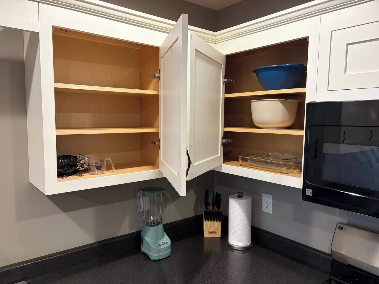 A kitchen with open cabinets, a blender, a knife block, and a microwave.