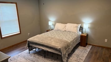 Een slaapkamer met een bed, twee bedlampen, een plafondventilator, een raam met zonwering en een houten vloer.