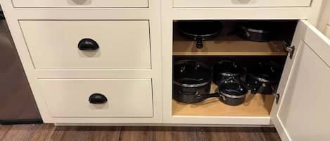 Une cuisine avec trois tiroirs et un placard contenant des casseroles et des poêles.