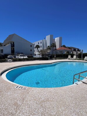 Piscina com aviso de profundidade de 1,8 metros, cercada por um deck pavimentado e com um edifício ao fundo.