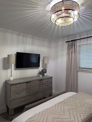 Een slaapkamer met een bed, een kapstok, een televisie en een plafondlamp.