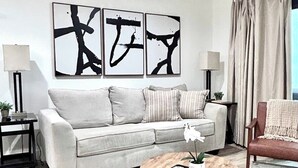 A living room with a sofa, a coffee table, and abstract art on the wall. - 30A Style! Private Beach | Chair Service Included (Seagrove)