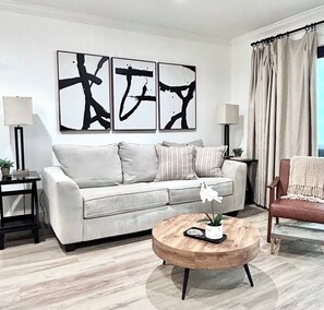 Uma sala de estar com sofá, mesa de centro e arte abstrata na parede.