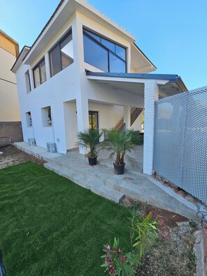 Uma casa moderna de dois andares com telhado plano, janelas amplas e varanda coberta.