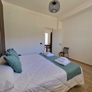 Quarto de hotel com uma cama grande, uma cadeira e vista para o corredor.