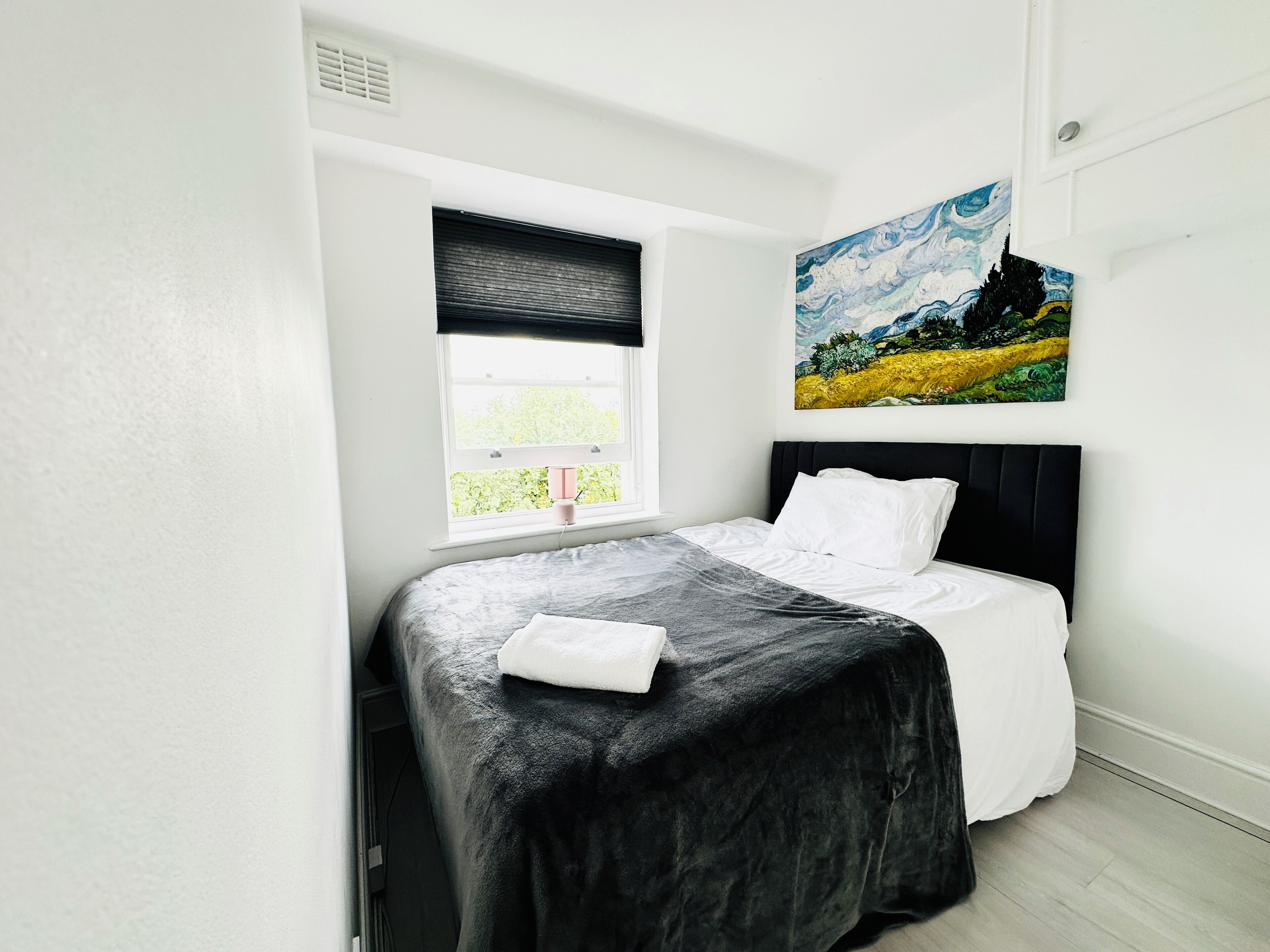 A bedroom with a bed, a window, and a painting on the wall.