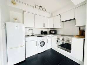 A modern kitchen with white cabinets, a built-in washing machine, a microwave, and a stove. - Mons Sanctus - Warrick Ave, a sanctuary in the heavens (London)