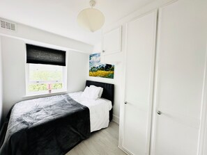 Een slaapkamer met een bed, een raam met uitzicht, een schilderij aan de muur en een deur.